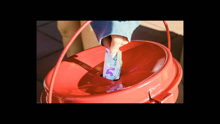 A person putting a $5 bill into a donation bucket.