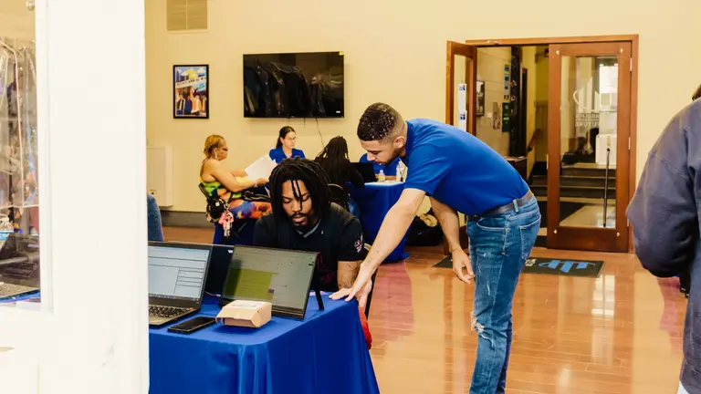 A person sits at a table while someone leans over his shoulder