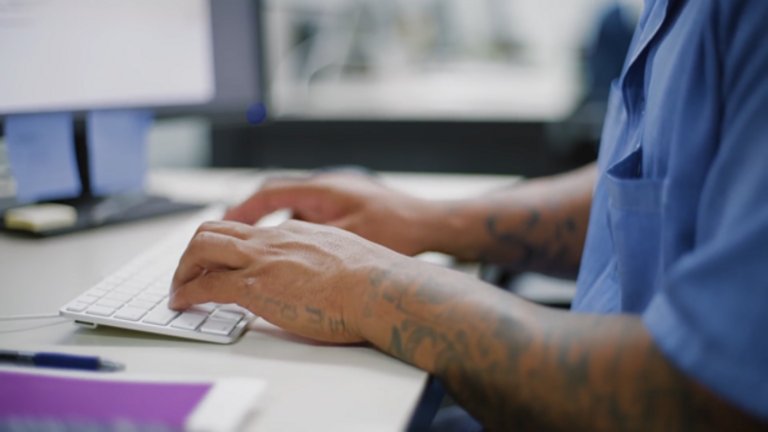Former inmate with tattooed arms typing on a keyboard, participating in a prison reentry program to support their transition back into society.