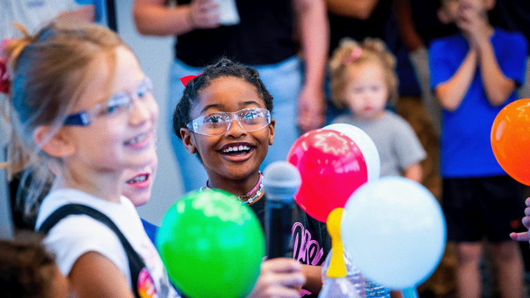 Students wearing science googles holding colorful balloons