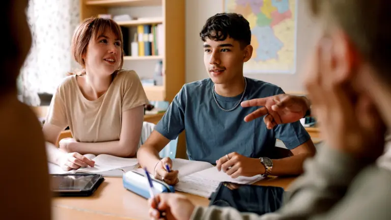 A woman with red hair and bangs sitting at a table next to a guy with brown hair wearing a blue tee shirt