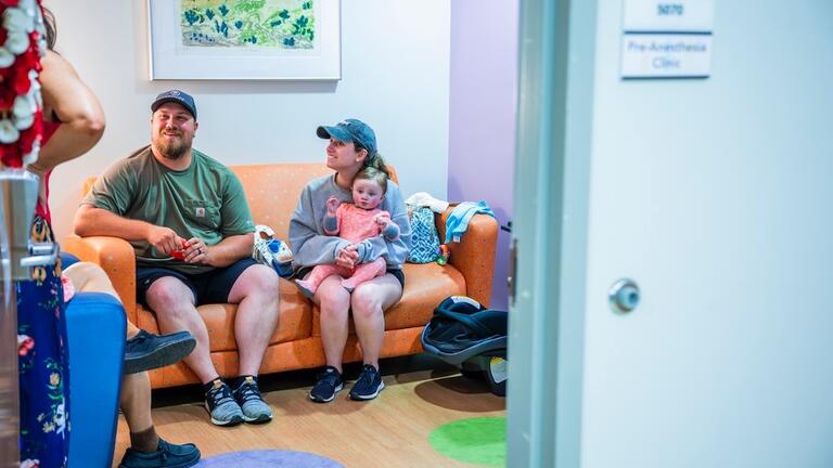 A family sits with their child on a couch in a hospital clinic room.