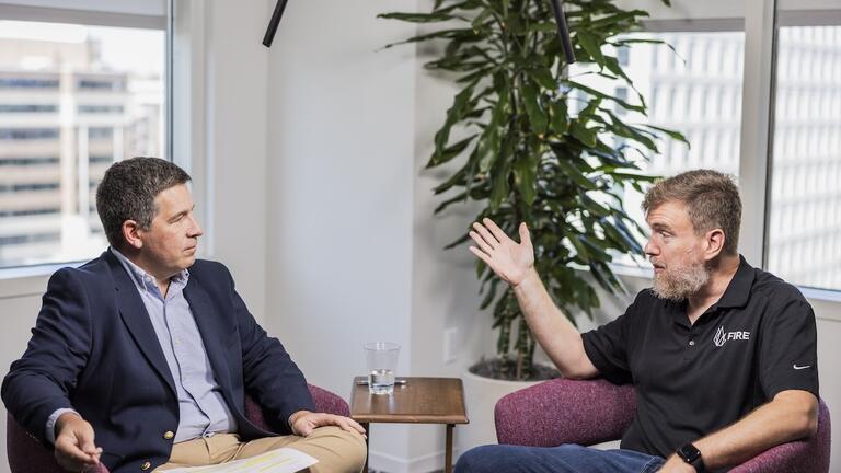 Two individuals engage in civil discourse in a modern office, with microphones overhead capturing their discussion.