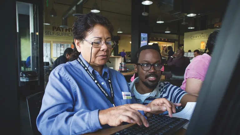 Two individuals collaborate at a computer in a workforce center, highlighting community-driven efforts to bridge the skills gap.