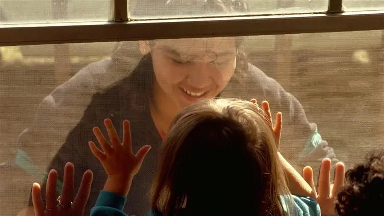 A smiling mother looking through the window at her children.