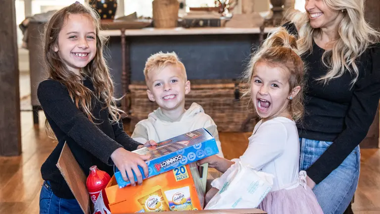 children and a women smiling for a photo as they take toys out of a box