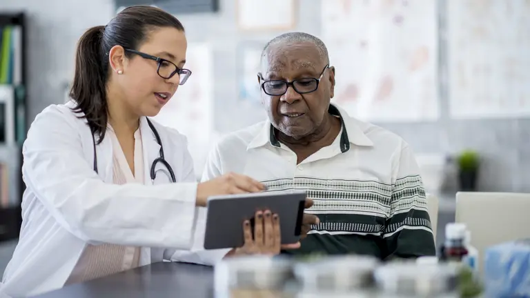 A doctor explains something on a tablet to an older gentleman
