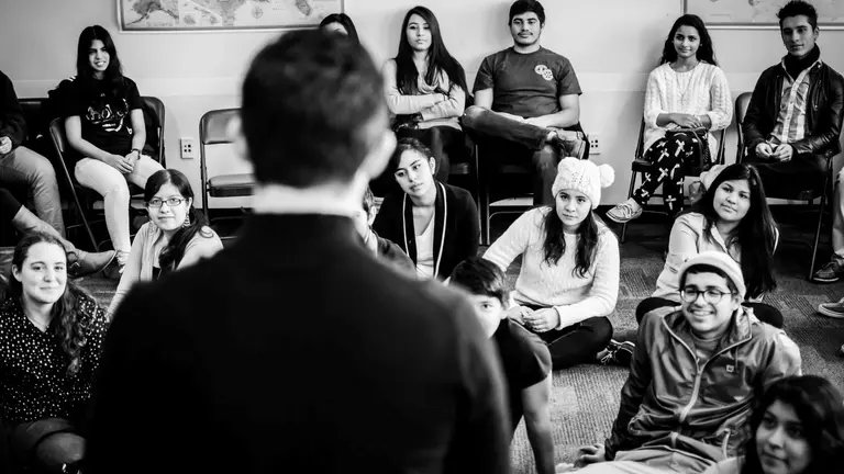 A black and white photo of a group of youth listening to a speaker