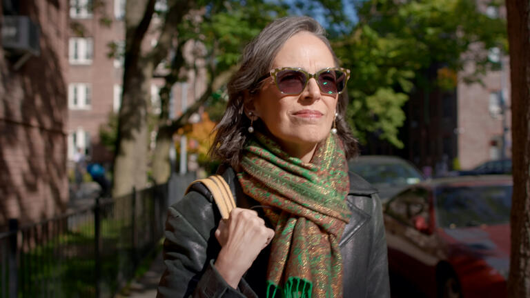 Lenore Skenazy outside wearing sunglasses looking into the distance facing the sunlight