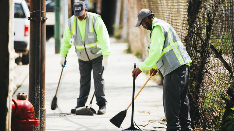 Two people cleaning up the street with brooms and dustpans