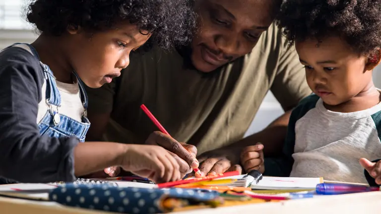 A man helps two children with school work