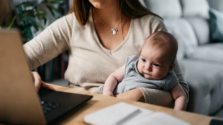 A woman on a laptop holding a baby