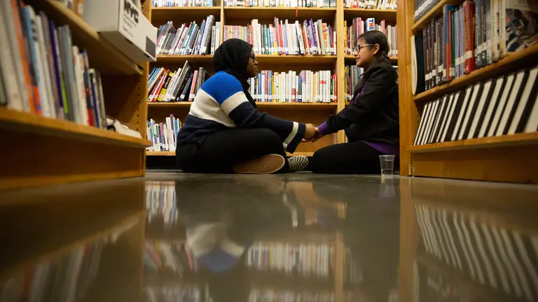 Two students sitting holding hands in a library