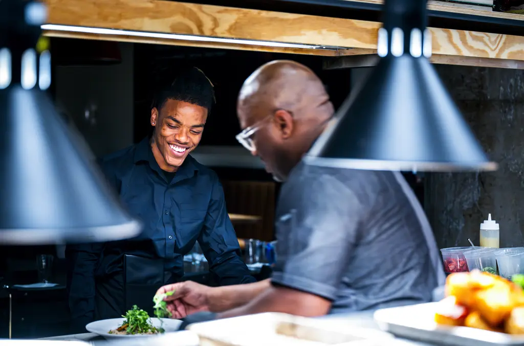 Chef guides intern as they prepare a dish.