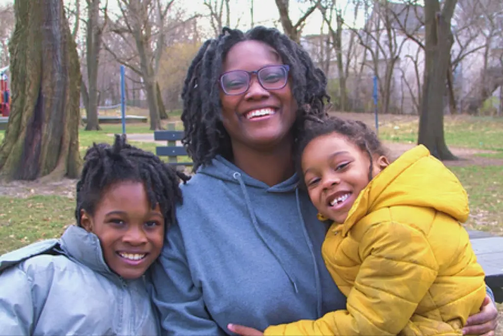 A smiling mother holding her children at the park.