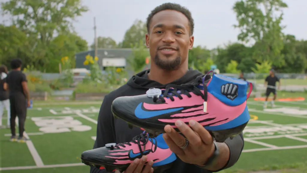 Derrick Barnes on a football field holding his cleats.