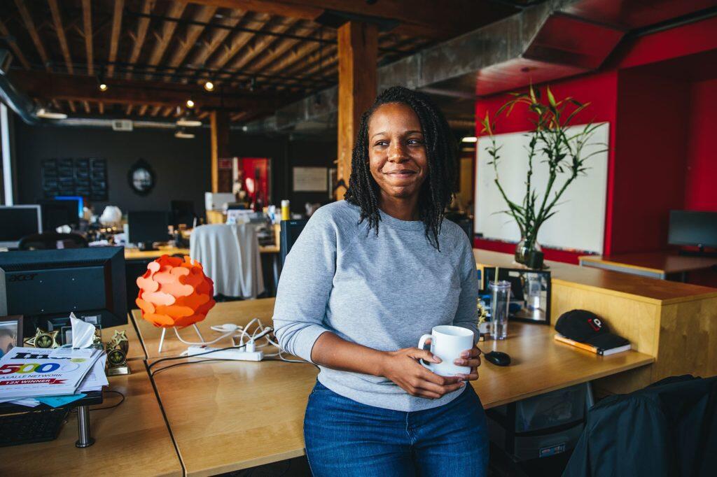 Amber Williams, Alumni, i.c.stars smiling sitting on the edge of a desk holding a mug
