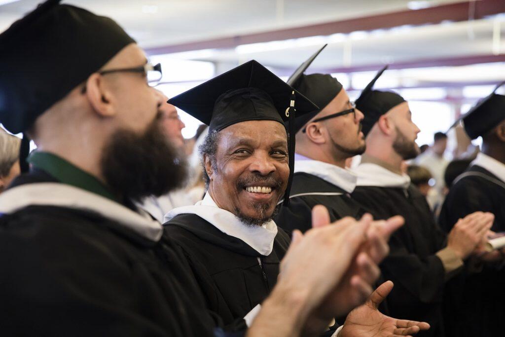 A group of men in caps and gowns clapping and smiling