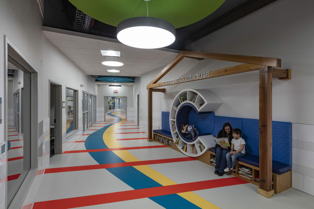 A woman sits with a child reading a book in a school hallway