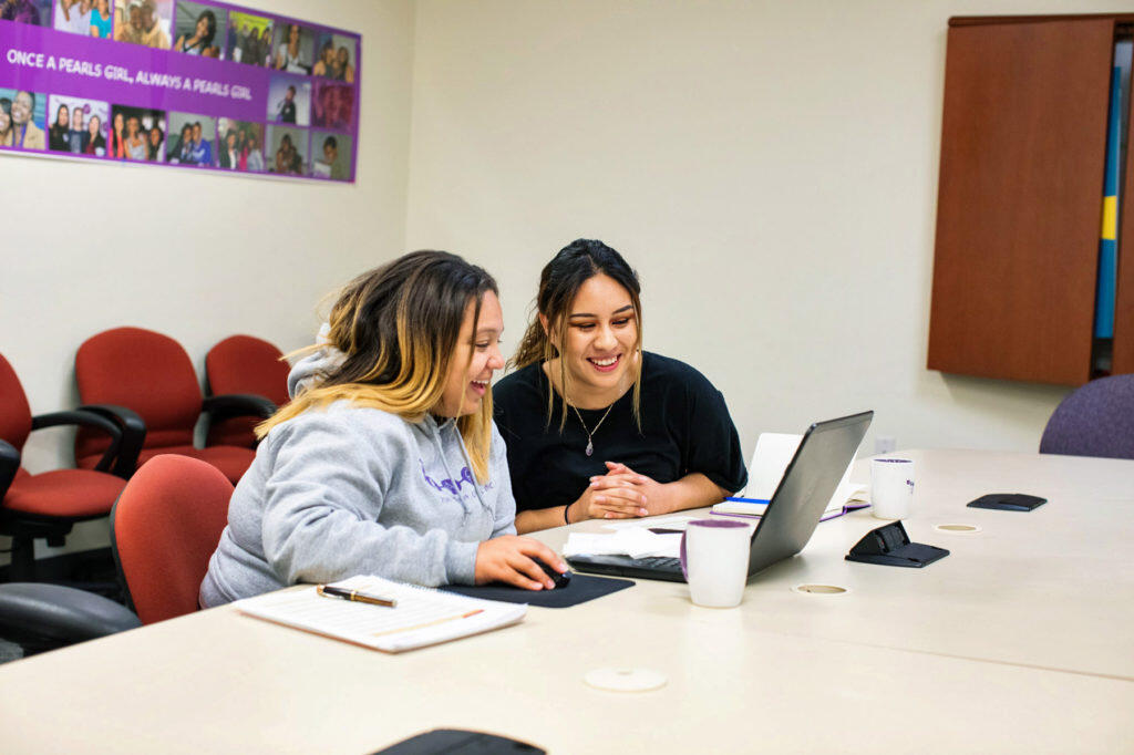 Two young women work on laptop together