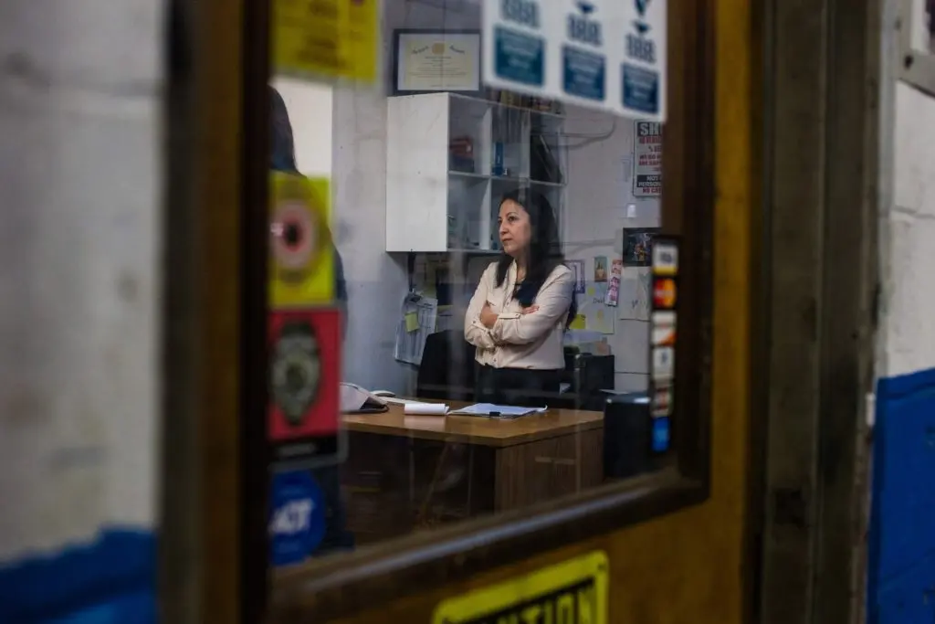 Hilda stands behind a desk in the office of an auto shop