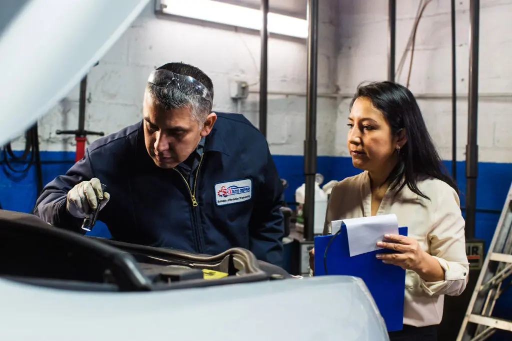 Jose inspects under the hood of a car while Hilda watches