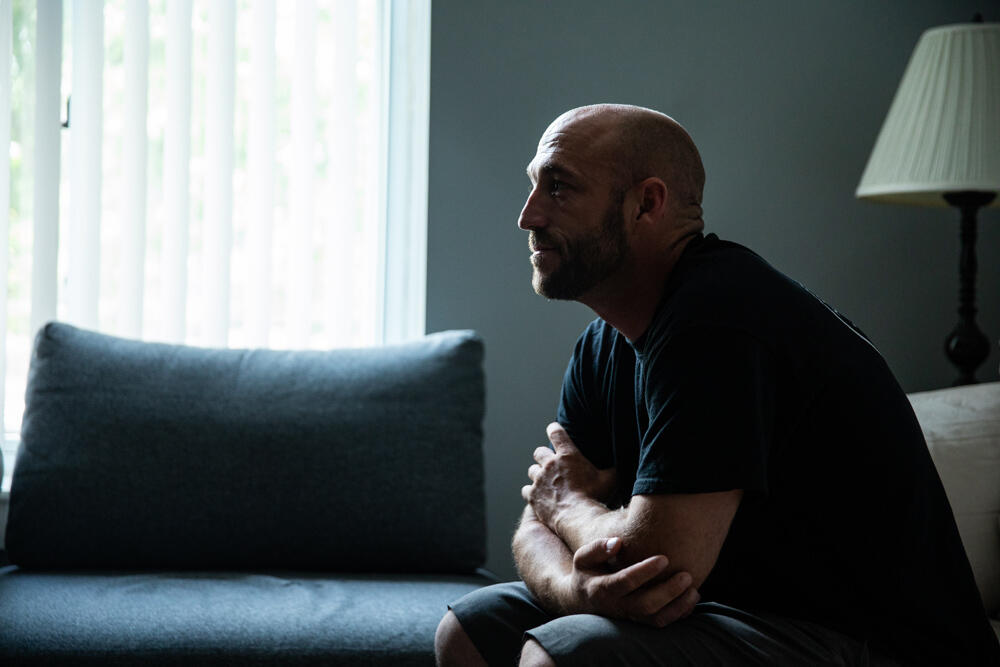 A man with a tattoo on his arm sits on a couch