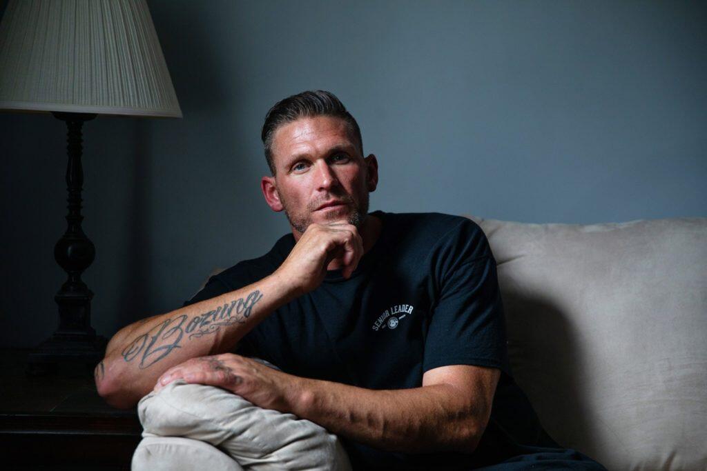 A man with a tattoo on his arm sits on a couch