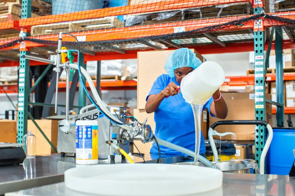 A woman pours a bucket of soap into a bowl