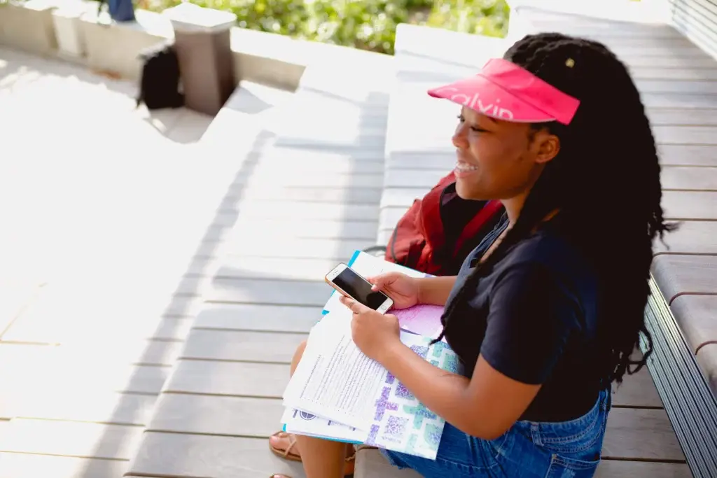 Gaby, a moneythink student, sitting down on her phone with school work in her lap