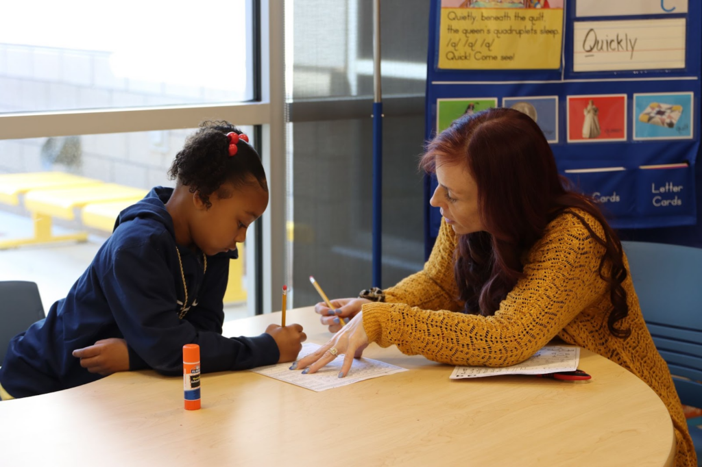 Young girl and teacher writing at a table.